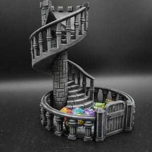 Peut inclure: Un escalier en colimaçon gris imprimé en 3D avec une petite porte. L'escalier est rempli de dés colorés, parfait pour les jeux de société. La conception présente des pierres détaillées et une esthétique de château classique.