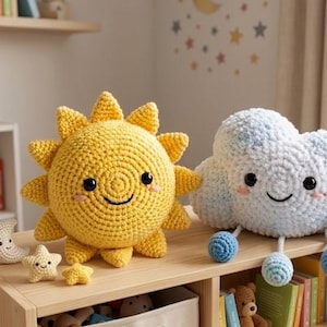 May include: A crocheted yellow sun and a white and blue cloud with smiling faces. The sun has spiky rays, and the cloud has blue dangling accents. Small crocheted stars and a moon are also present, suggesting a nursery theme.