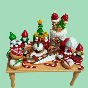 Puede incluir: Una escena navideña en miniatura sobre una pequeña mesa de madera. La escena incluye gorros de Papá Noel, hombres de jengibre, renos, árboles de Navidad, rosquillas y bastones de caramelo. Las figuras son de colores brillantes con detalles en rojo, verde, blanco y dorado.