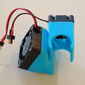 May include: A small fan assembly in black and blue, with red and black wires and connectors. The fan is mounted on a blue plastic bracket. Designed for cooling electronic components.