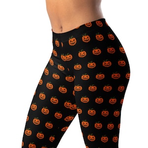 Può includere: Leggings neri con un motivo ripetuto di zucche di Halloween arancioni con volti intagliati. Le zucche presentano piccioli verdi ed espressioni frastagliate dall'aspetto luminoso, disposte in una griglia regolare su tutto il tessuto.