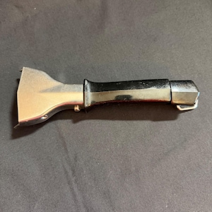 May include: A metal and black handle tool, likely for a specific purpose. The tool has a shiny, silver-colored head with a curved design and a black, rectangular handle. The tool is on a dark background.