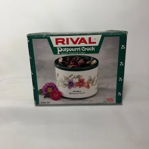 May include: A Rival Potpourri Crock electric simmering cooker in its original packaging. The box features a white stoneware crock with a floral pattern, filled with dried potpourri. Text includes RIVAL Potpourri Crock, 3206 PP, and Quality Stoneware.