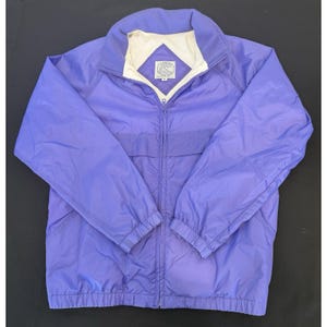 May include: A lavender-colored jacket with a full zipper closure. The jacket has a stand-up collar with a white and cream-colored lining. The jacket has two front pockets and the brand logo is visible on the collar.