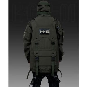 Puede incluir: Chaqueta t&aacute;ctica verde oscuro con m&uacute;ltiples bolsillos, correas y capucha. La chaqueta presenta las letras "H-G" en un rect&aacute;ngulo blanco en la espalda. La chaqueta est&aacute; dise&ntilde;ada con una est&eacute;tica futurista de inspiraci&oacute;n militar.