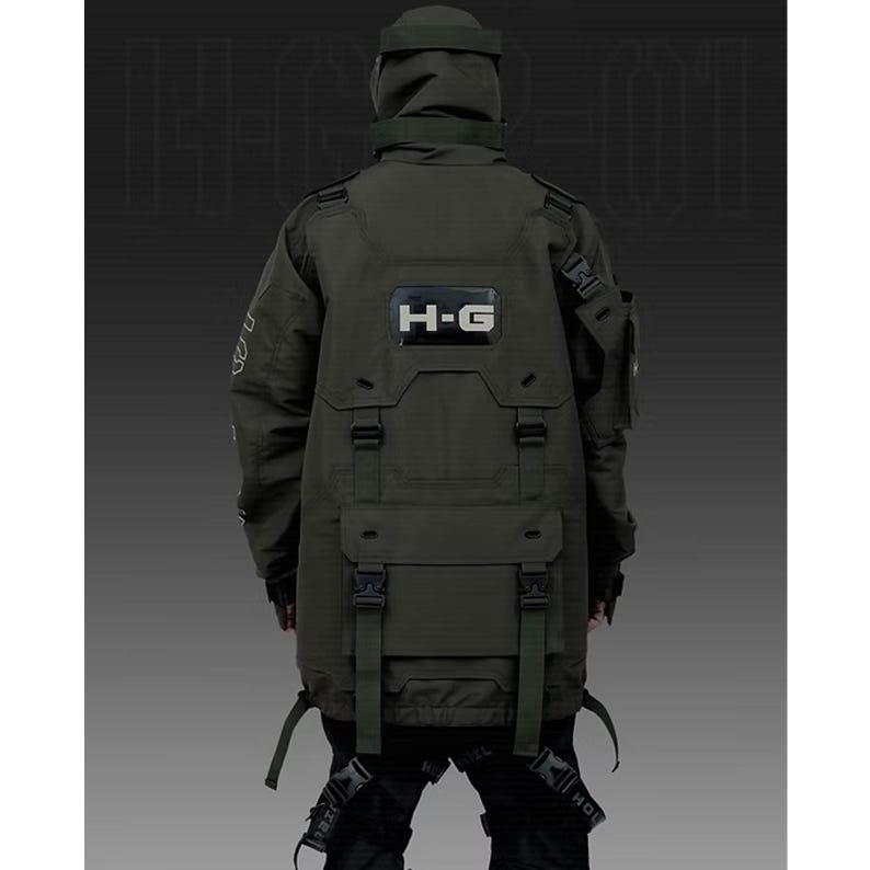 Puede incluir: Chaqueta t&aacute;ctica verde oscuro con m&uacute;ltiples bolsillos, correas y capucha. La chaqueta presenta las letras "H-G" en un rect&aacute;ngulo blanco en la espalda. La chaqueta est&aacute; dise&ntilde;ada con una est&eacute;tica futurista de inspiraci&oacute;n militar.