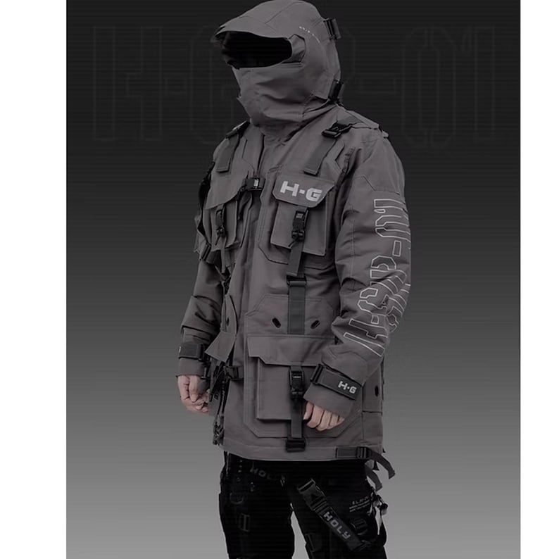 Puede incluir: Chaqueta t&aacute;ctica gris con m&uacute;ltiples bolsillos, correas y una capucha que cubre la cara. La chaqueta tiene el texto "H-G" en el pecho y el brazo. La chaqueta es parte de un atuendo futurista de estilo urbano.