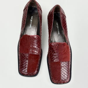 Peut inclure: Une paire de mocassins rouge foncé avec un bout carré et un design à textures mixtes. Les chaussures combinent un motif gaufré façon peau de serpent et des empiècements en fourrure à poils ras. Les semelles intérieures portent le texte Sergio Rossi.