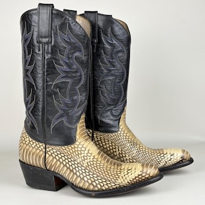 Può includere: Un paio di stivali da cowboy con gambale in pelle nera con cuciture decorative blu e piede in pelle testurizzata con motivo a pelle di serpente color crema e marrone chiaro. Gli stivali presentano punta affusolata, tacco e linguette superiori.