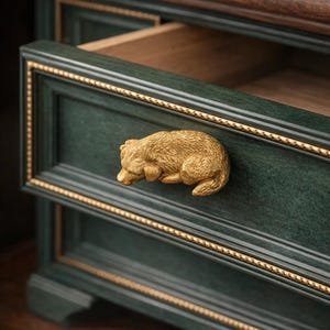 May include: Close-up of a dark green drawer with a gold bear-shaped handle. The drawer has gold trim and is partially open, revealing a wooden interior. The furniture has a classic, elegant design.