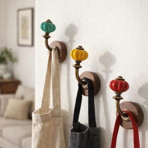 Puede incluir: Tres ganchos de pared decorativos con pomos de cerámica en forma de calabaza de colores. Los ganchos están montados sobre bases redondas de madera y sostienen bolsas de mano. Los pomos son turquesa, amarillo y rojo.