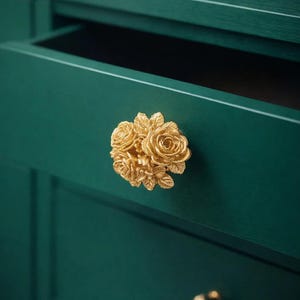 以下が含まれることがあります： 濃い緑色のキャビネットに、金色の花の形をした引き出しの取っ手。引き出しは部分的に開いており、内部が見えます。小さな丸い金のノブが下にあります。