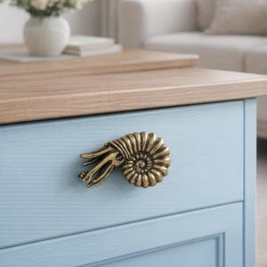 Peut inclure: Un meuble bleu clair avec un dessus en bois et une poign&eacute;e d&eacute;corative en forme de coquillage nautile de couleur laiton. Le meuble est un &eacute;l&eacute;ment d'un meuble plus grand, comme une commode ou une table de chevet.