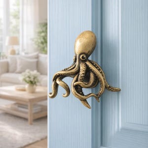 Op de afbeelding: Een bronzen deurklink in de vorm van een octopus, gemonteerd op een lichtblauwe deur. Het octopusontwerp heeft gedetailleerde tentakels en een getextureerd oppervlak, wat een unieke nautische touch geeft.