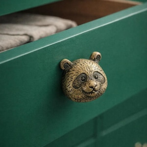 Peut inclure: Gros plan sur un tiroir vert avec un bouton en forme de panda en laiton. Le tiroir est ouvert, révélant un aperçu de l'intérieur. Le bouton panda a des détails et une expression souriante.