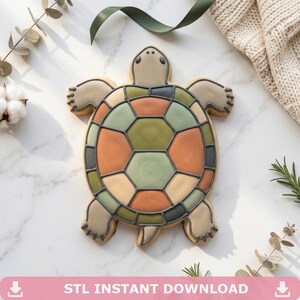 May include: A turtle-shaped biscuit with a colourful shell design. The shell features geometric patterns in shades of orange, green, and grey. The biscuit is decorated with brown icing and has a light beige body. The image includes the text "STL INSTANT DOWNLOAD".