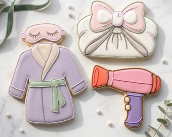 May include: Cookies shaped like spa day items. Includes a lavender robe, a pink sleep mask, a white purse with a pink bow, and a pink and orange hairdryer. The text "STL INSTANT DOWNLOAD" is at the bottom of the image.