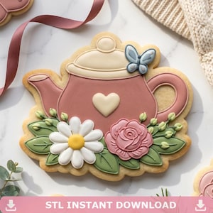 Peut inclure: Un biscuit en forme de théière rose, décoré d'un cœur blanc, d'un papillon et de motifs floraux. Le biscuit présente une marguerite et une rose, avec des feuilles vertes. Le texte "STL INSTANT DOWNLOAD" est en bas.