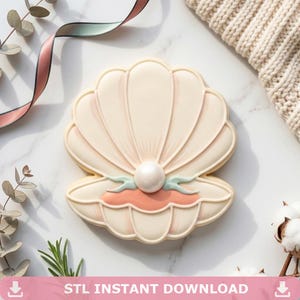 May include: A seashell-shaped cookie with a pearl in the center. The cookie is decorated with light pink, peach, and light blue accents. The text "STL INSTANT DOWNLOAD" is at the bottom of the image.