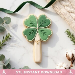 May include: A St. Patrick's Day-themed cookie shaped like a four-leaf clover. The cookie has green icing with leaf details and a white and gold stem. The text "STL INSTANT DOWNLOAD" is at the bottom of the image.
