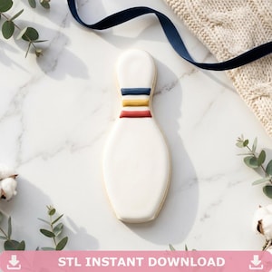 Könnte beinhalten: Ein bowlingkegelförmiger Keks mit weißer Glasur und drei horizontalen Streifen in Blau, Gelb und Rot. Der Keks liegt auf einer Marmoroberfläche mit einem marineblauen Band und einem Strickpullover. Text "STL INSTANT DOWNLOAD".