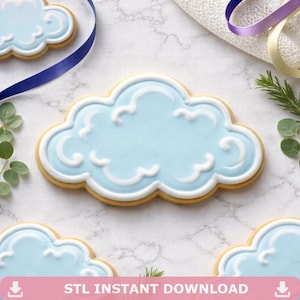 Può includere: Biscotti a forma di nuvola con glassa azzurra e decorazioni a spirale bianche. I biscotti hanno una base marrone chiaro e sono disposti su una superficie di marmo. L'immagine include anche un nastro blu e del verde.