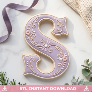 May include: A letter S shaped biscuit decorated with smooth lavender icing and intricate white and light pink piped scrollwork and floral details. The biscuit features a clean, defined edge and a flat surface, showcasing detailed icing artistry.