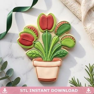 以下が含まれることがあります： 鉢植えのハエトリグサの形をしたデコレーションクッキー。クッキーは薄いベージュ色の鉢、鮮やかな緑色の茎と葉、そして濃い赤色と明るい緑色の色合いで、ギザギザの縁がはっきりと見える複数の捕虫葉で構成されています。