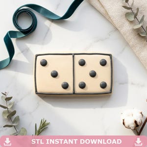 Op de afbeelding: Een koekje in de vorm van een domino, met een beige achtergrond en zwarte stippen. De domino heeft een zwarte rand en de tekst "STL INSTANT DOWNLOAD" in een roze banner onderaan.
