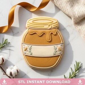 Puede incluir: Una galleta con forma de tarro de miel con una base marrón claro y una tapa amarilla. La galleta tiene una pancarta blanca con diseños de abejas y hojas. El texto "STL INSTANT DOWNLOAD" está en la parte inferior de la imagen. Una cinta dorada y ramitas de romero y algodón están en el fondo.