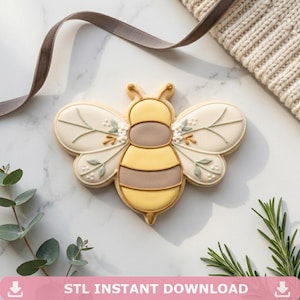 May include: A bee-shaped cookie with yellow, brown, and white icing. The wings are decorated with floral and leaf designs. The cookie is on a marble surface. Text at the bottom reads "STL INSTANT DOWNLOAD".