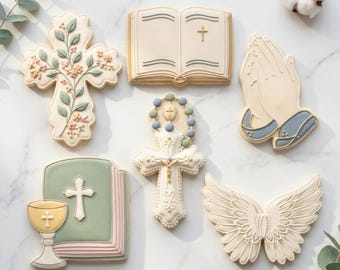 May include: Assortment of decorated cookies in religious themes. Includes a cross with floral accents, an open book with a cross, praying hands, a rosary, a chalice with a book, and angel wings. The cookies are in shades of white, beige, green, and blue.