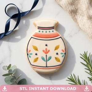 May include: A decorated sugar cookie in the shape of a vase. The cookie is beige with orange, teal, yellow, and navy blue details. The cookie has a floral design and the text "STL INSTANT DOWNLOAD" at the bottom.