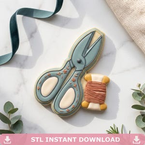 Può includere: Un biscotto a forma di forbici da cucito in stile vintage color blu tenue con accenti crema e piccoli dettagli floreali, accompagnato da un biscotto più piccolo a forma di rocchetto di filo con estremità giallo senape e filo color pesca.