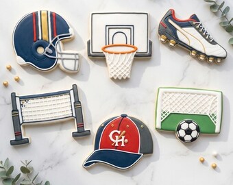 May include: Assortment of sports-themed cookies, including a football helmet, basketball hoop, soccer cleat, volleyball net, baseball cap, and soccer goal with a ball. The cookies are decorated with various colors and details.