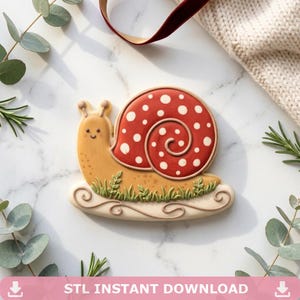 May include: A snail-shaped cookie with a red and white spotted shell, a tan body, and green grass detail. The cookie sits on a white, swirled base. The text "STL INSTANT DOWNLOAD" is at the bottom of the image.