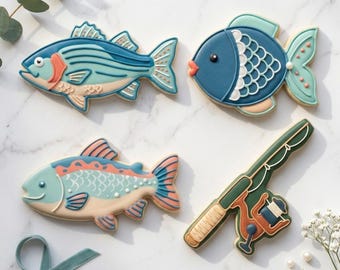 May include: Four fish-shaped cookies and a fishing rod cookie. The fish cookies are decorated with blue, peach, and white icing. The fishing rod cookie is green, brown, and orange. The text "STL INSTANT DOWNLOAD" is at the bottom of the image.
