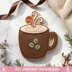 May include: A coffee mug shaped cookie decorated with brown icing, featuring three light green coffee bean accents on the front and cream colored icing on top with swirling steam details. The text STL INSTANT DOWNLOAD is visible.