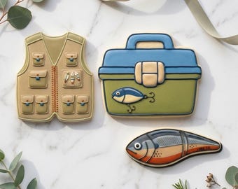 May include: Cookies in the shape of a fishing vest, tackle box, and fish. The vest is tan with pockets and a zipper. The tackle box is blue and green with a fish graphic. The fish cookie is silver, orange, and gray. Text at the bottom reads "STL INSTANT DOWNLOAD".