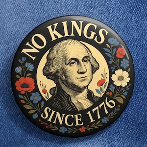 Puede incluir: Un botón redondo negro con el texto "NO KINGS SINCE 1776" que rodea un retrato de George Washington. El botón está decorado con detalles florales rojos, azules y blancos y está prendido a una chaqueta vaquera azul.