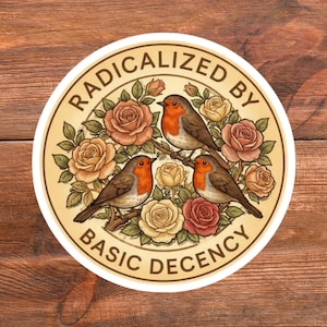 Puede incluir: Pegatina redonda con borde crema. Presenta tres petirrojos posados en una rama, rodeados de rosas crema, melocotón y rojas. El texto "RADICALIZED BY BASIC DECENCY" está dispuesto en círculo.