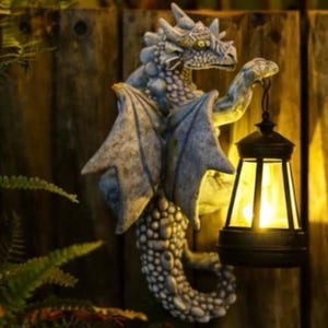 Puede incluir: Estatua de dragón gris con alas extendidas y una linterna. El dragón está montado en una valla de madera. La linterna es negra con luz amarilla.