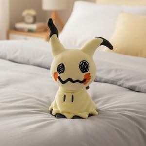 May include: A Mimikyu plush toy, with a pale yellow body and a black, jagged mouth. The toy has black eyes and orange cheek markings. The ears are yellow with black tips. The toy is placed on a gray bed.