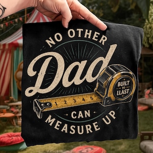 May include: Black t-shirt with a vintage design featuring the words "NO OTHER Dad CAN MEASURE UP." A yellow tape measure and the words "BUILT TO LAST" are also included in the design.