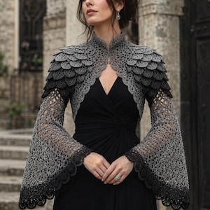 May include: A black sleeveless dress paired with a grey and black crocheted bolero. The bolero features a high collar, layered scale-like textures on the shoulders, and long, flared bell sleeves with an intricate openwork pattern and scalloped edges.