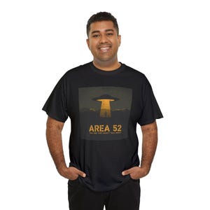 May include: Black t-shirt featuring a graphic of a UFO hovering over a desert landscape with a cactus. The text "AREA 52" and "THE ONE THEY WON'T TALK ABOUT" are printed in gold.