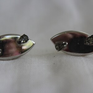 May include: A pair of silver earrings with a teardrop shape and two small black rhinestones on each earring.