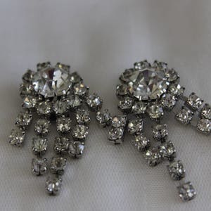 May include: A pair of silver tone earrings with a large clear rhinestone in the center and smaller rhinestones cascading down the sides.