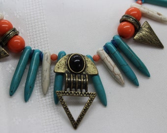 May include: A turquoise, white, and orange beaded necklace with a gold pendant featuring a black stone and a triangular design.