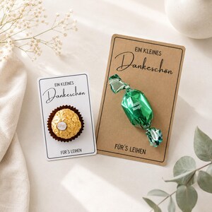 Op de afbeelding: Twee kleine cadeaubonnen met de woorden "Ein Kleines Dankeschön" erop gedrukt. Eén kaart bevat een goud omwikkelde chocolade, de andere een groen snoepje. De zin "Für's Leihen" staat op beide kaarten.